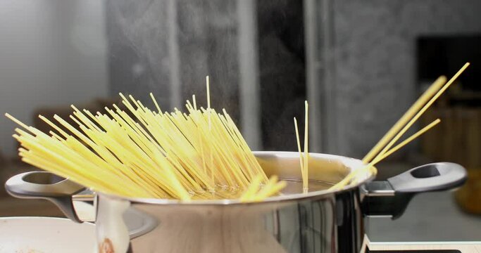 Spaghetti is dipped into a pot of boiling water. cooking pasta. hot water steam. food preparation in the kitchen. front view. close-up. 