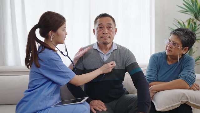 Asian female physician cardiologist listening heartbeat and checking lungs of mature middle aged man and explaining heart condition system on tablet
