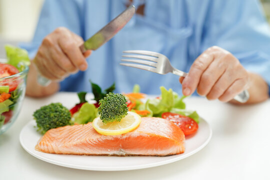 Asian Elderly Woman Patient Eating Salmon Stake And Vegetable Salad For Healthy Food In Hospital.