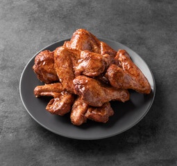 Roasted chicken wings bbq on a gray plate on a dark background. The concept of snacks for the menu. Free space for text.