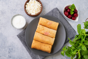 Homemade crepes with cherry berry and a cottage cheese on a plate on a blue background with mint. Healthy food for the breakfast.