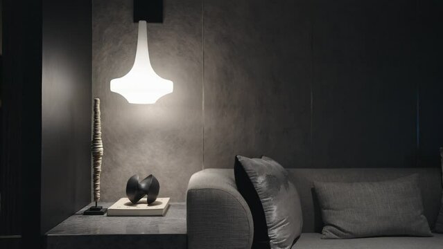 The light from lamp in modern living room at night. Living room in gray and black colors. Design in minimalist style. Modern design of living room