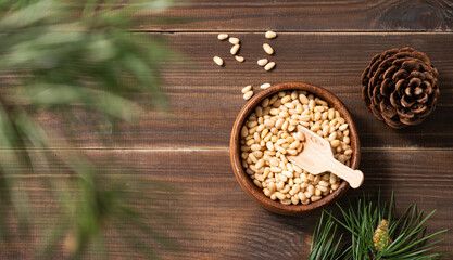 Obraz na płótnie Canvas Pine nuts in a bowl on a dark wooden background with branches of pine needles and cone. The concept of a natural, organic and healthy superfood and snack.