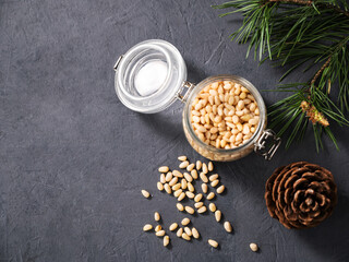 Obraz na płótnie Canvas Pine nuts in a jar and a scattered on a dark background with branches of pine needles and cone. The concept of a natural, organic and healthy superfood and snack.
