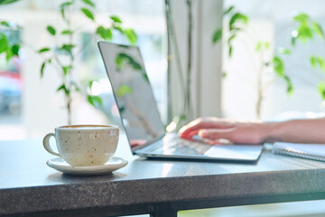 Close-up of cup with coffee on table, background is laptop, hands of man typing