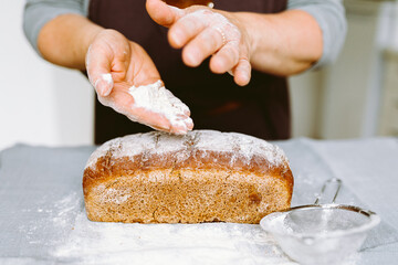 Woman baker hands hold baked homemade floured bread