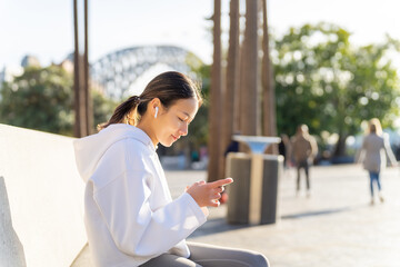 Fototapeta premium Asian woman in sportswear listening to music from earphones with mobile phone app during jogging exercise at city street in the morning. Healthy girl do sport training running workout in the city.