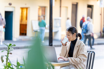 Young Asian woman freelance enjoy working business or creative job on laptop computer at outdoor cafe in the city. Digital nomad people working from anywhere on digital device and wireless technology.