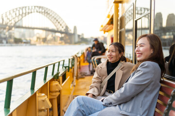 Fototapeta premium Happy Asian woman friends sitting on ferry boat crossing Sydney harbour in Australia. Attractive girl enjoy and fun urban outdoor lifestyle shopping and travel in the city on holiday vacation.