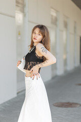 Cool fashionable young beautiful woman model in summer outfit with fashion lace top and bra with white skirt and handbag walks in the city