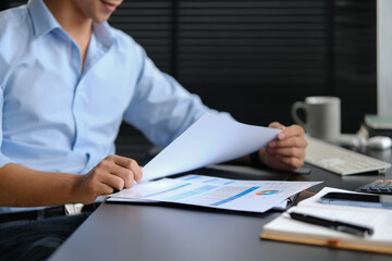 Young businessman in blue shirt preparing report and analyzing work results at office desk