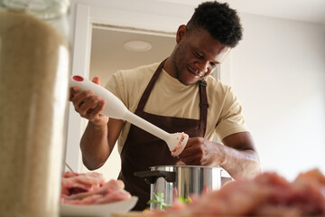 Young black man using a blender to prepare chicken mince in a kitchen.