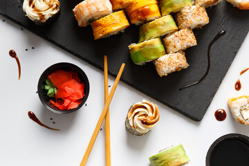 Flat lay of various sushi rolls placed on stone board with chopsticks and soy sauce on gray...
