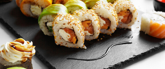 Flat lay of various sushi rolls placed on stone board with chopsticks and soy sauce on gray background © Наталья Марная
