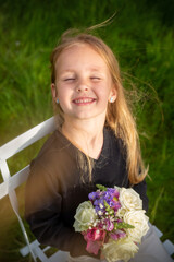 Portrait of a girl in the rays of the sun on a white chair on the background of a green garden