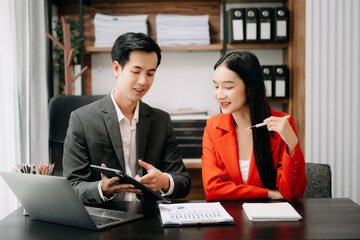 Asian business colleague business presents and explains and using laptop and tablet. Teamwork, financial marketing team,   while sitting in office room.