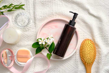 Unlabeled pump bottle placed on marble tray with white flowers. A brush, cushion compact, scented candle and a glass of water displayed. Cleansing product advertising
