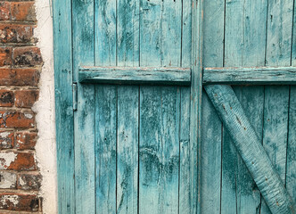 A part of closed vintage turquoise wooden hinged shutters on the wooden window in the old red brick wall with copy space. Peeling paint. Grunge background.