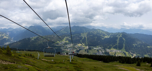 Cable cars and cabins in Alpine lanscape with French Alps ski town Les Gets in the background during summer. Outdoor mountainous sports. Wide panorama Belvedere view