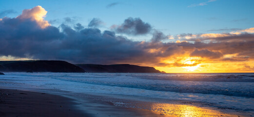 Fototapeta na wymiar Dramatic sunset with waves breaking on Widemouth Beach in Cornwall, UK