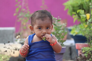 Cute indian baby girl eating a leaf in the garden.