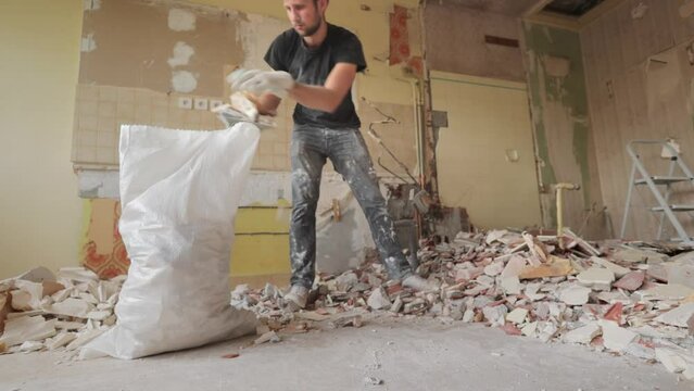 Male worker cleaning up renovation site indoor with a shovel inside a rubble bag