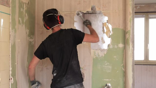male contractor punching a hole in wall with small sledge hammer during renovation