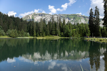 Impressive rock formations rising above the pine tree forest surrounding French mountainous meltwater Gold Mines Lake near Morzine village