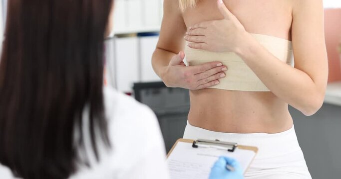 Woman with elastic bandage on her chest showing breast doctor to mammologist 4k movie. Mammoplasty surgical treatment of breast cancer concept