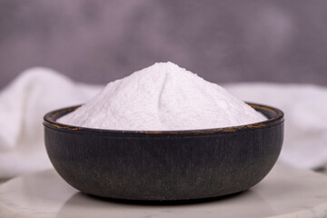 Sodium bicarbonate or baking soda on grey background. Sodium bicarbonate powder in bowl. Close up