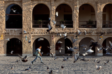 Doha, Qatar - February 01 2023:  motion photo for A boy runs around a carrier pigeon in Souq Waqif