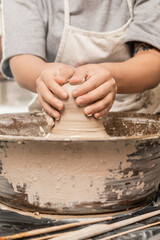 Cropped view of blurred and tattooed craftswoman in apron molding wet clay while working on pottery wheel near tools on table in ceramic studio, clay sculpting process concept