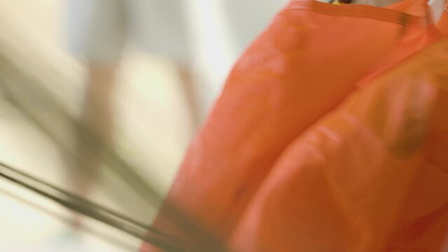 Close-up of a person's hands folding an orange parachute.