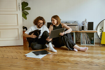 Couple sitting on floor and stroking cats while listening music on vinyl player with records
