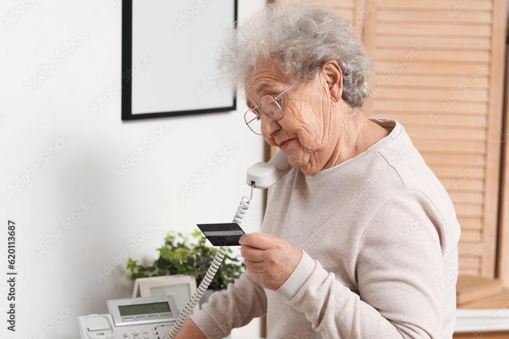 Sticker Senior woman with credit card talking by telephone at home