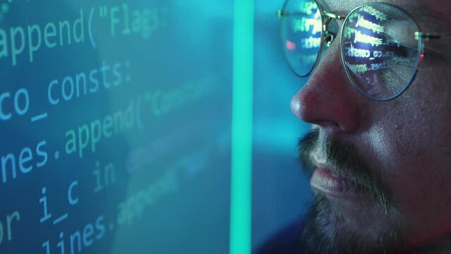 Close-up image of male face, programmer, software developer looking on digital screen with coding information. Code reflection on glasses. Concept of profession, occupation , IT, modern technologies