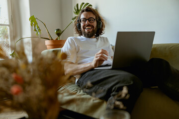 Smiling man using laptop for online learning or watching movie while lying on sofa at home