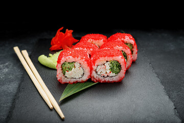 Sushi roll with crab sticks, cream cheese, cucumber, and caviar on a black background with ginger and wasabi