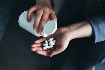 Fototapeta premium Woman Pours Medical Pills or Tablets into her palm from Pill-Bottle, close-up. Disease Healing or Dietary Nutritional Supplement, Medication.