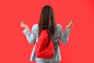 Female student with backpack making heart shape on red background, back view