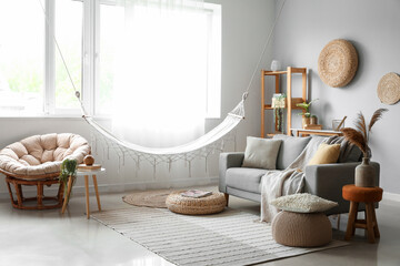 Interior of light living room with hammock, grey sofa and armchair