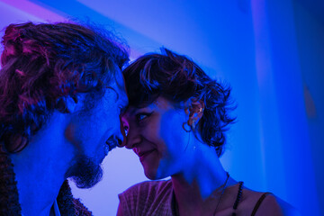 Young lovers in blue and purple neon light looks at each other with desire. Guy and girl together...