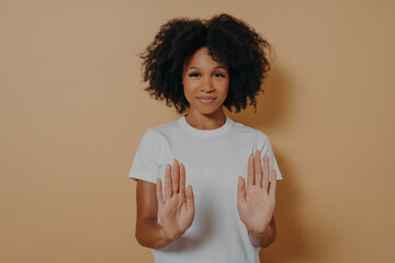 Young smiling mixed race woman with curly hairstyle raising palms in stop or prohibition gesture