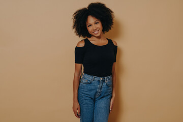 Pretty afro american woman looking at camera with shy charming smile againt dark beige wall