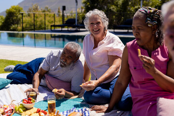 Happy senior diverse people sitting on blanket and having picnic in garden