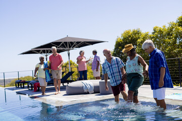 Happy senior diverse people spending time by swimming pool together in garden