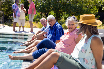 Happy senior diverse people sitting by swimming pool and smiling in garden