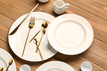 Clean plates, golden cutlery and pitchers on wooden table