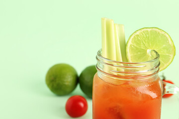 Mason jar of bloody mary with celery and lime on green background
