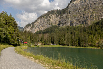 Walking path along Lac Montriond seen from above. Aerial of French Alps mountain range melt water lake in summer.